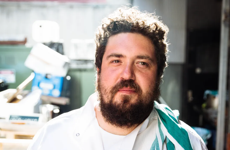 Adelaide chef Duncan Welgemoed of Africola wearing a white chef jacket with a striped towel over his shoulder for a close-up promo portrait.